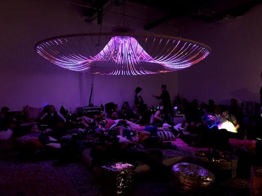 A photo of the chandelier on display, lit up in purple, with visitors below